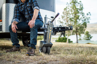 Grey Trailer Valet 5X Dolly attached to a trailer with person in jeans and a flannel sitting on the tongue of the trailer.