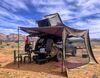 SUV with roof tent and car awning with blue sky and buttes in the background.