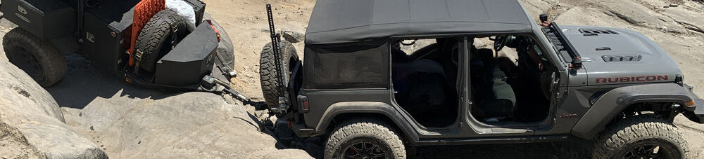 Jeep pulling an overlanding trailer over boulders.