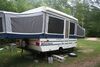 White pop-up camper popped up sitting in the middle of a wooded area.