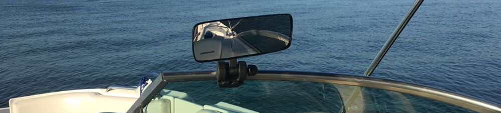 Rearview boat mirror mounted on boat windshield of boat floating in the water.