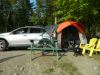 SUV in the woods with a tent attached to the trunk and a picnic table and chairs set up outside.