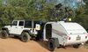 White Jeep pulling a white teardrop camper with trees in the background.