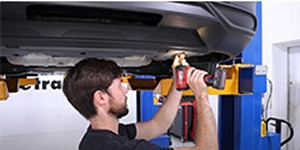 Installer securing a trailer hitch with a power drill under a lifted vehicle.