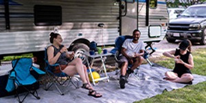 Friends relaxing outside their RV at a campsite.