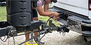 Person plugging trailer wiring into the back of a pickup truck.
