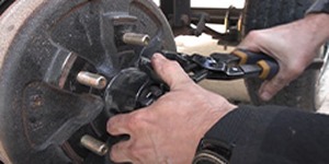Mechanic using pliers to service a trailer wheel hub.