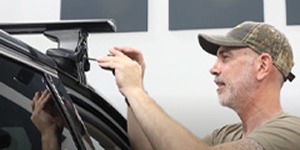 Installer securing a roof rack foot pack onto the side rail of a black SUV.