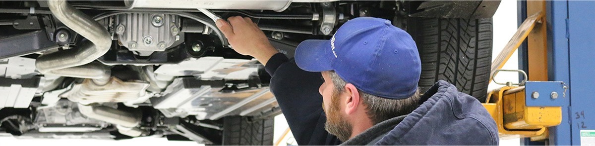 Mechanic installing a trailer hitch under a vehicle on a lift.