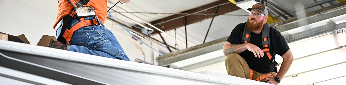 Technicians in safety harnesses working on the roof of an RV at a service shop.