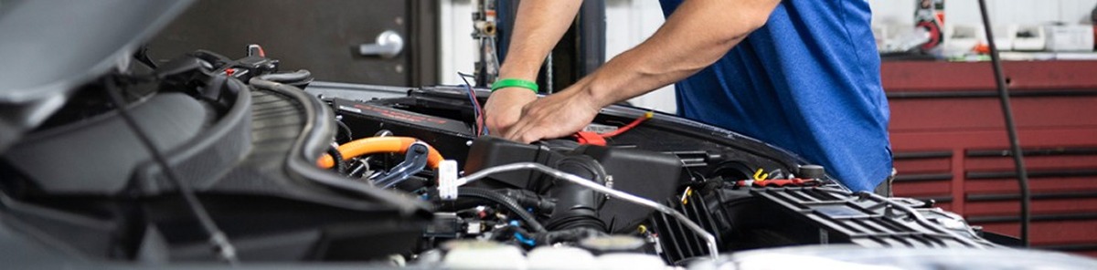 Technician installing towing accessory wiring under the hood of a vehicle.