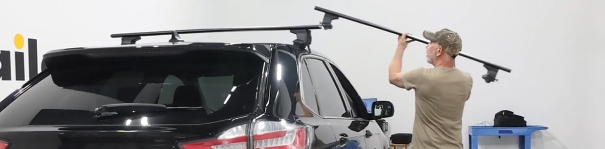 Installer mounting a roof rack crossbar onto the top of a black SUV inside a garage.