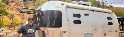 Man standing next to small airstream camper. 