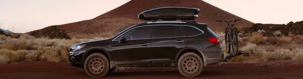 A car with a roof rack, roof box, and bike rack on a dirt road.